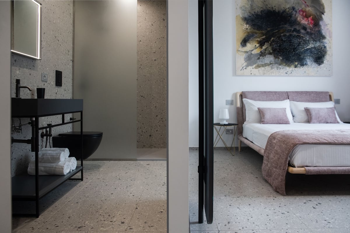 A modern bathroom with a black sink, a large bowl sink, and a shelf with towels.