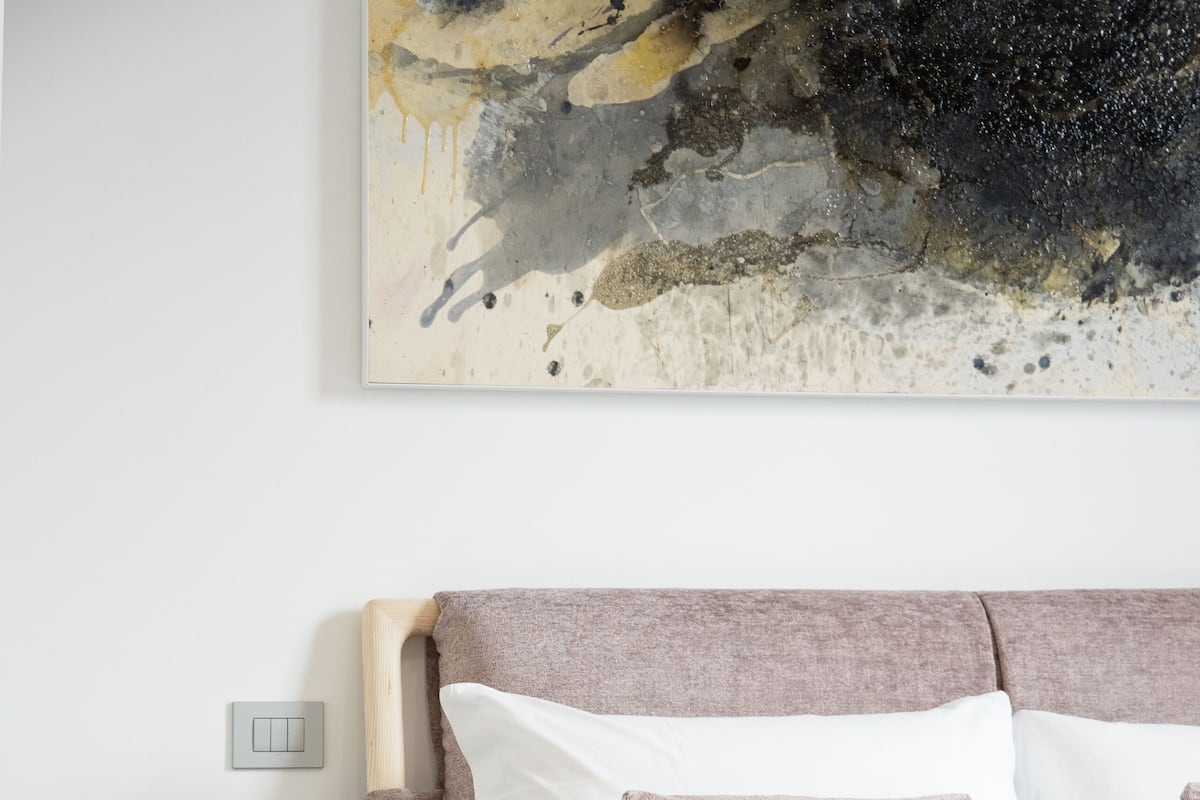 A bedroom with a bed, bedside table, lamp, and a painting on the wall.