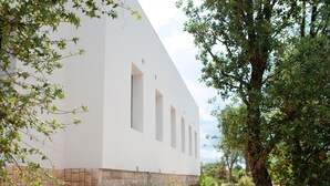Un edificio blanco con base de piedra, rodeado de follaje y un cielo despejado.