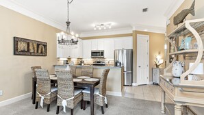 A modern kitchen with white cabinets, stainless steel appliances, and a dining area with wicker chairs and a chandelier. - Peninsula Links B102 (Gulf Shores)