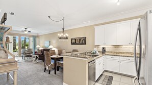 A spacious kitchen with white cabinets, a stainless steel refrigerator, and a dining area with a chandelier. - Peninsula Links B102 (Gulf Shores)