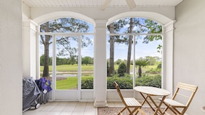 A covered patio with a view of a golf course, a grill, and folding chairs. - Peninsula Links B102 (Gulf Shores)