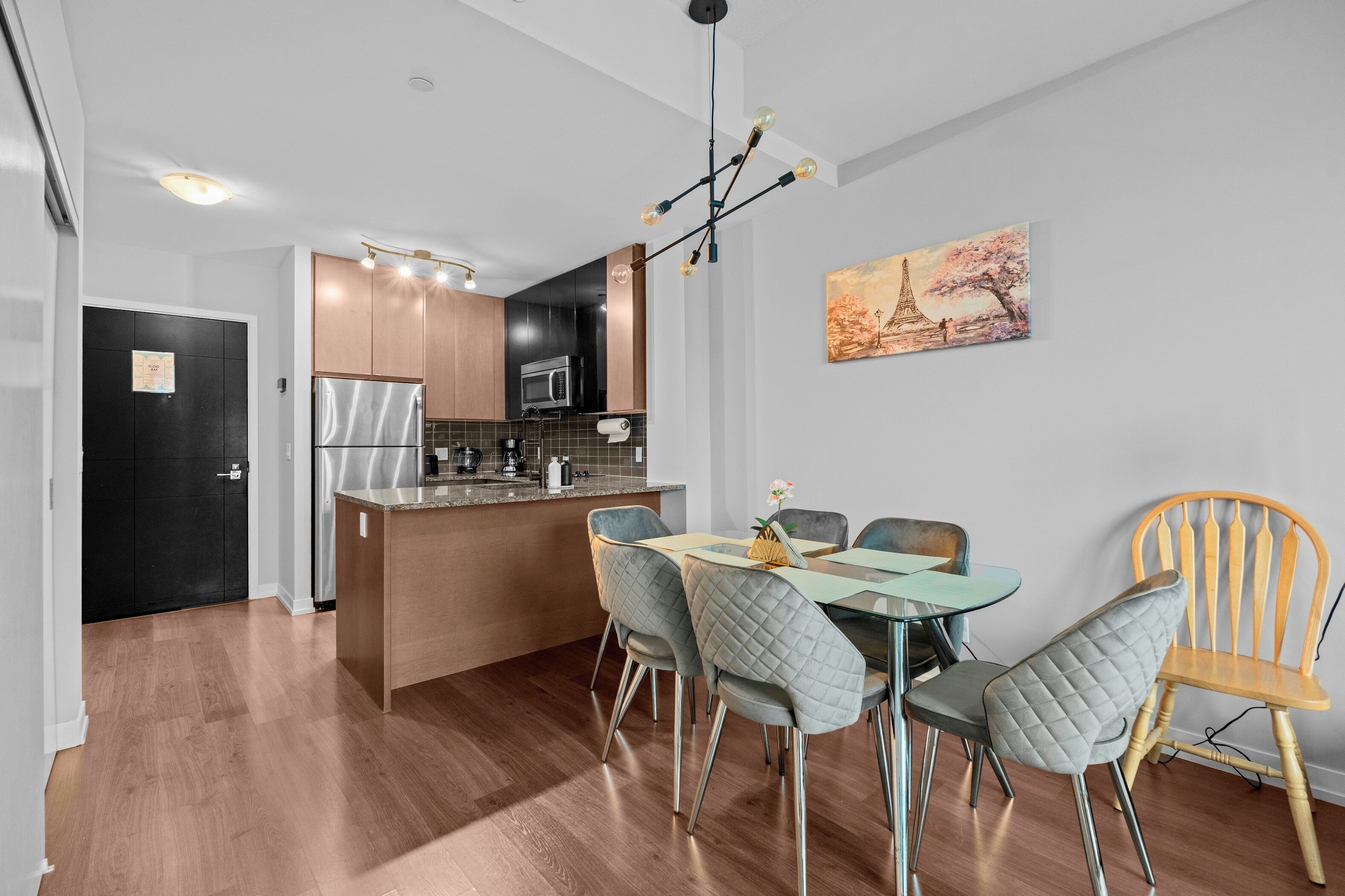 A modern kitchen with a central island, a dining area with a glass table and chairs, and a painting of the Eiffel Tower on the wall.