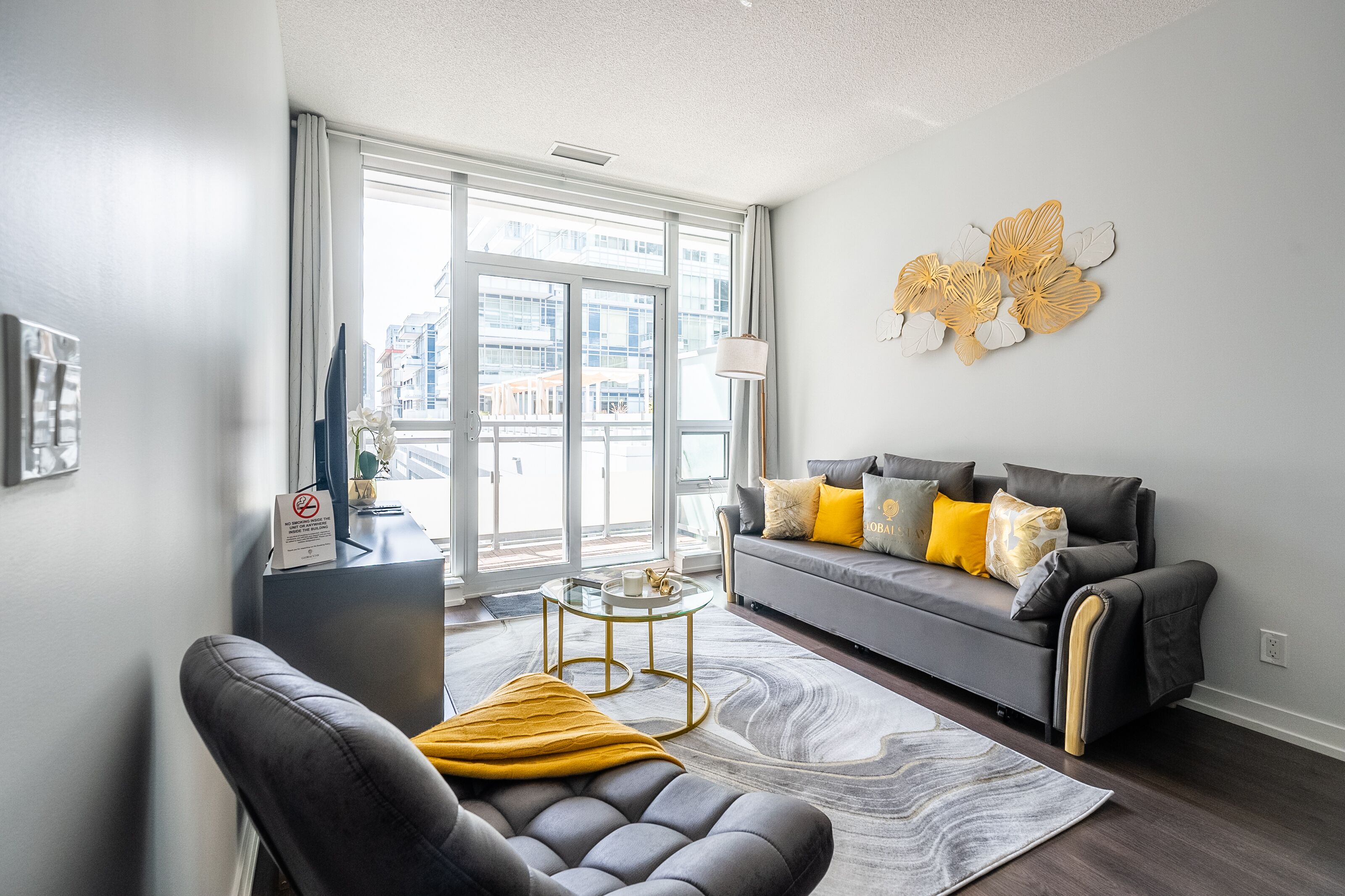 Ein modernes Wohnzimmer mit grauem Sofa, Ledersessel und Glastisch.