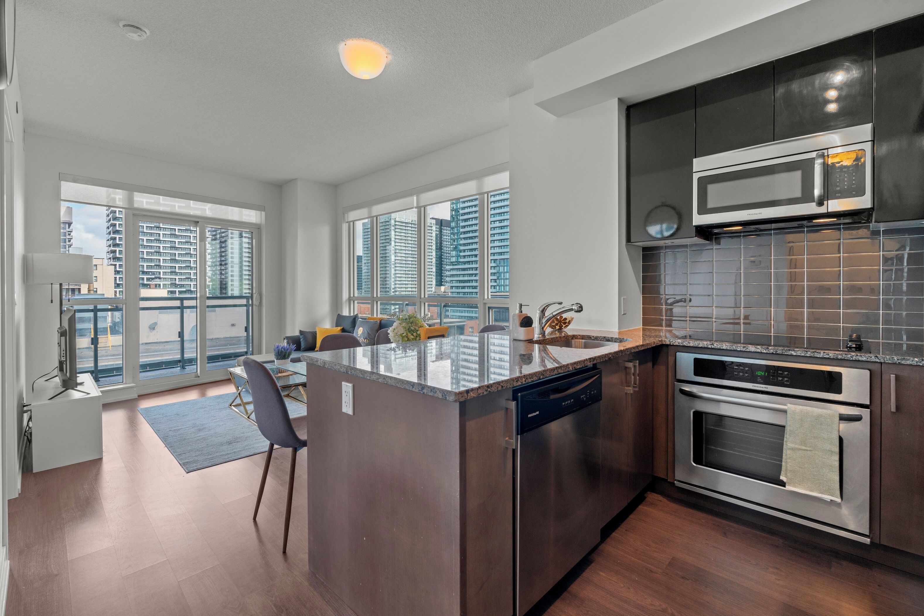A modern kitchen with a central island, stainless steel appliances, and large windows offering city views.