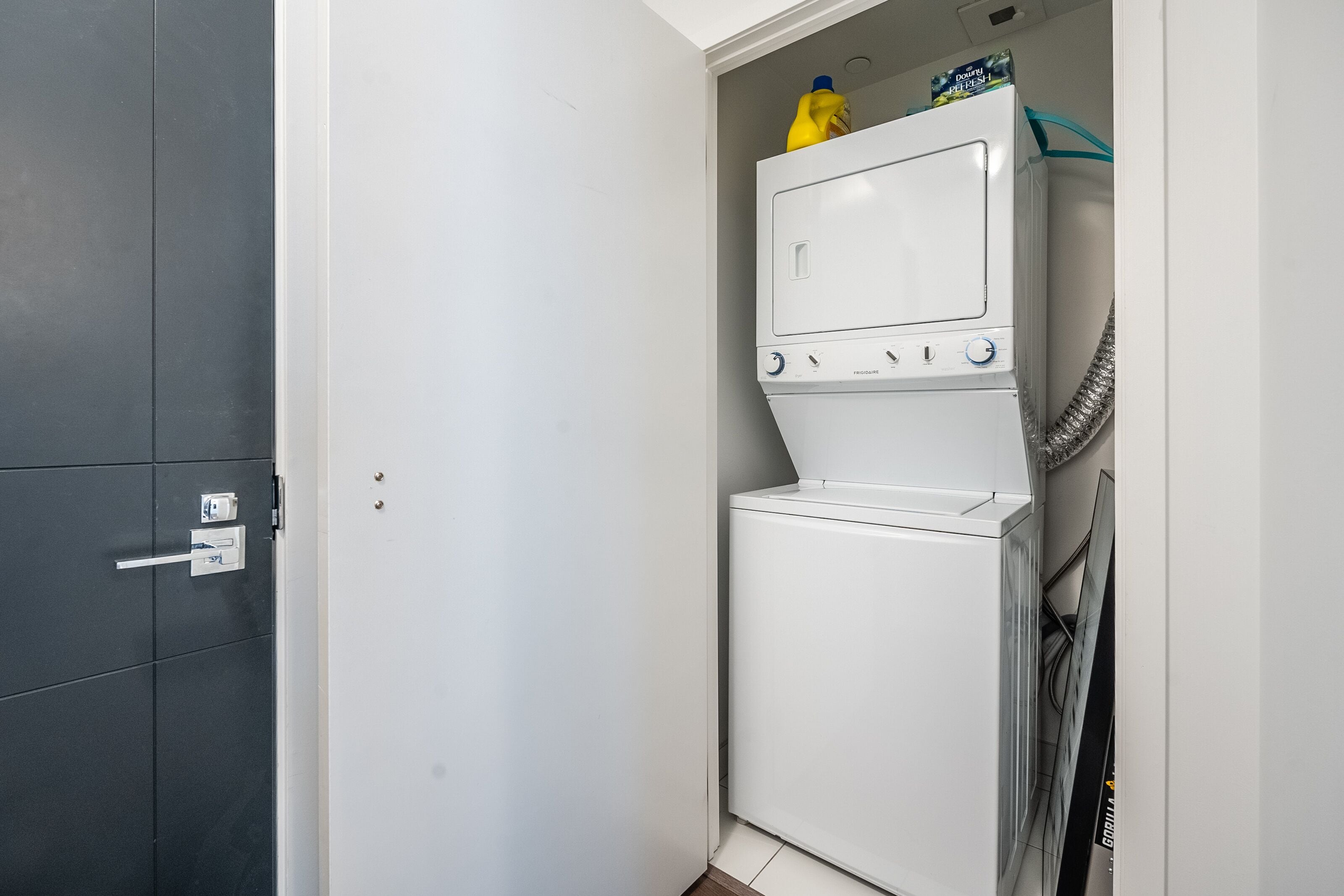 A laundry room with a washing machine and dryer, a door with a handle, and a small shelf with cleaning supplies.