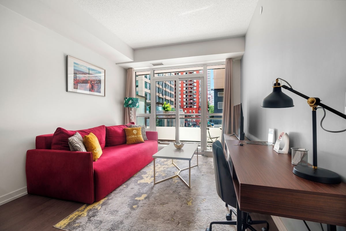 Ein modernes Wohnzimmer mit einem roten Sofa, einem Holztisch und einem großen Fenster mit Blick auf die Stadt.