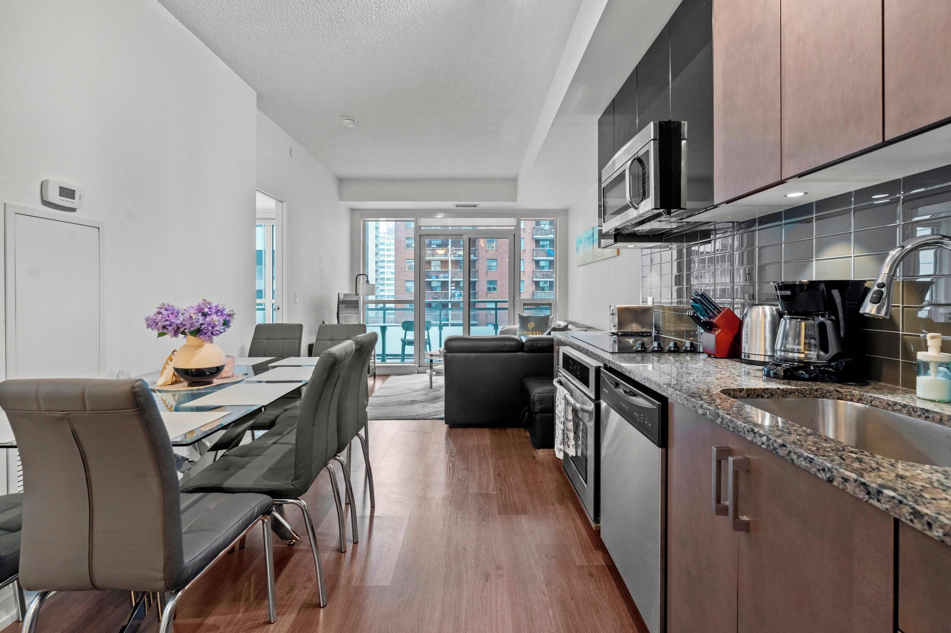 A modern kitchen with stainless steel appliances, a dining area with a table and chairs, and a view of a balcony with a cityscape.