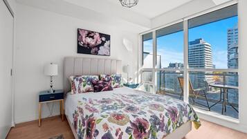 Un dormitorio moderno con una cama grande, una mesita de noche, una lámpara y vistas de la ciudad a través de amplias ventanas.