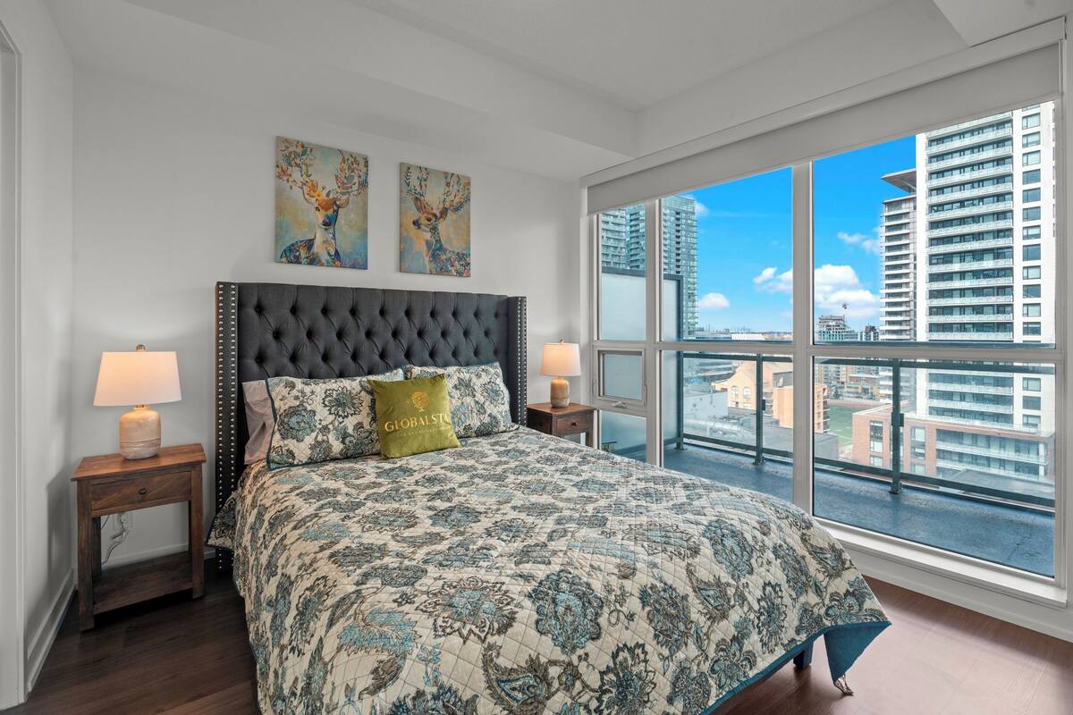 Ein Schlafzimmer mit einem großen Bett, zwei Nachttischen, einem Fenster mit Blick auf die Stadt und zwei Wandbildern.