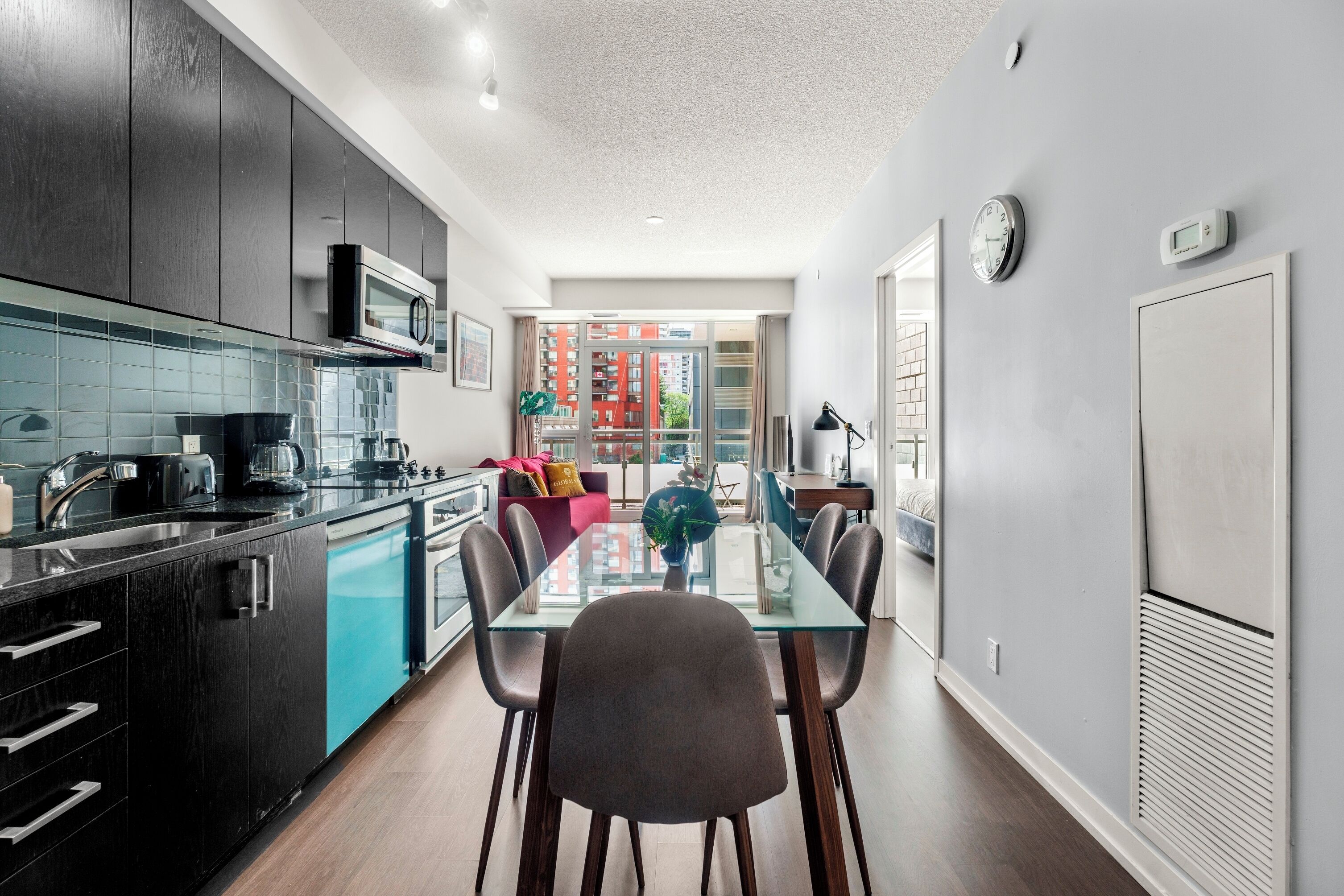 A modern kitchen with dark cabinetry, a glass dining table, and a view to a balcony.