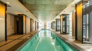 Una piscina interior larga con agua cristalina, rodeada de paredes con puertas y ventanas de vidrio, y un techo con iluminación empotrada.