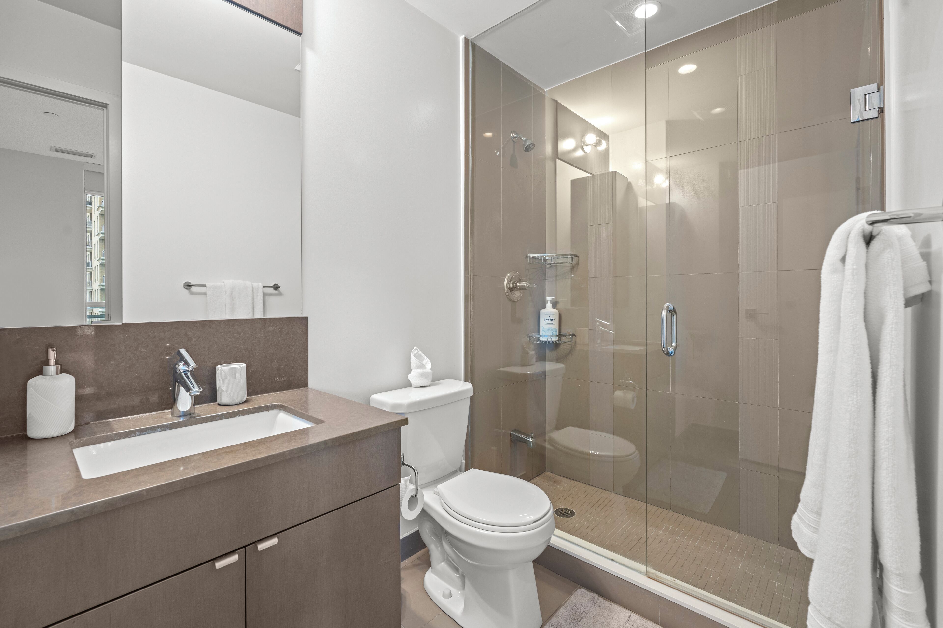 Un baño moderno con ducha de mampara de vidrio, lavamanos blanco y un inodoro.
