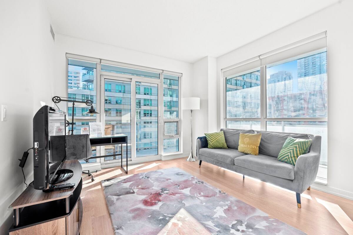 Ein modernes Wohnzimmer mit einer grauen Couch, einem Flachbildfernseher und einem großen Fenster mit Blick auf die Stadt.