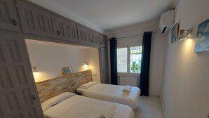 A hotel room with two beds, a stone headboard, a window with curtains, and a wall-mounted air conditioner. - 5 bedroom villa in l'escala (L'Escala)