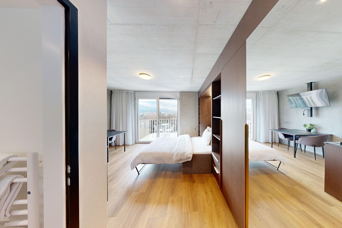 A modern hotel room with a balcony, a dining area, and a TV.