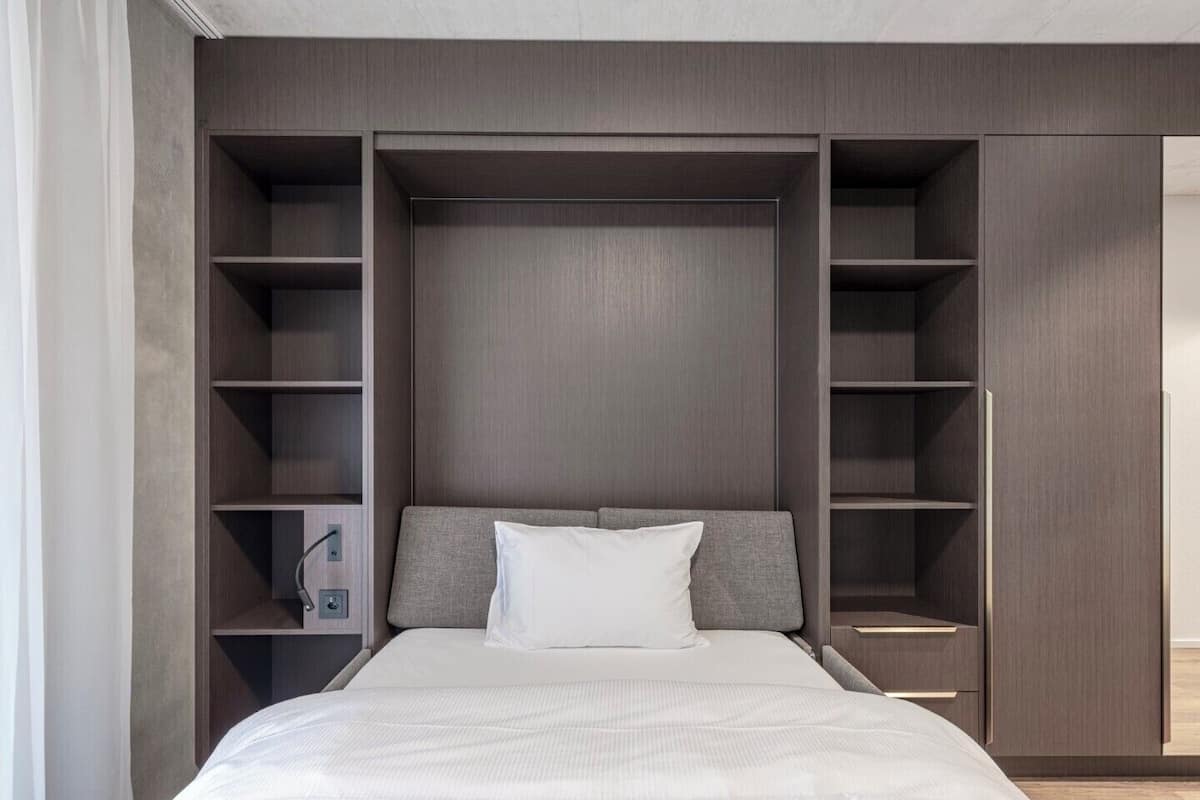 A bedroom with a bed, a nightstand, a wardrobe, and built-in shelving.