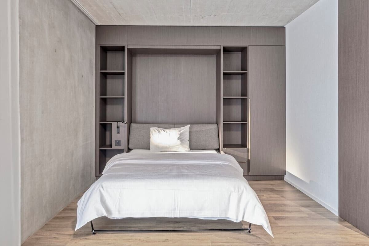 A modern bedroom with a bed, built-in shelving, and a concrete ceiling.
