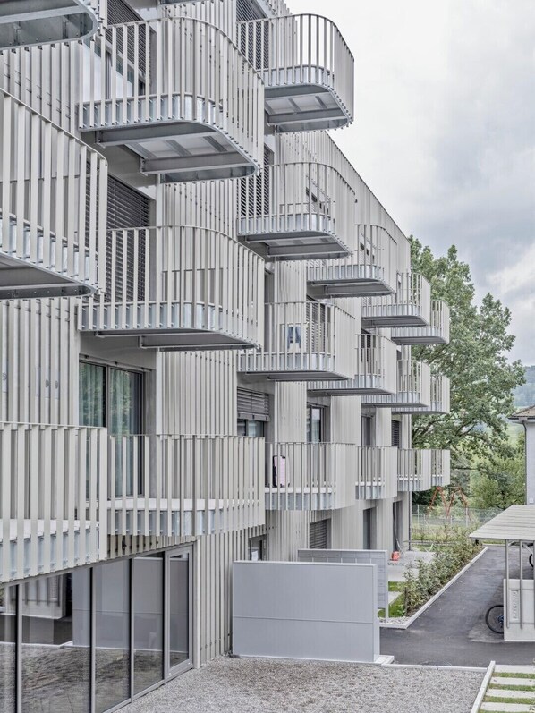 A modern building with multiple balconies, large windows, and a gravel ground.