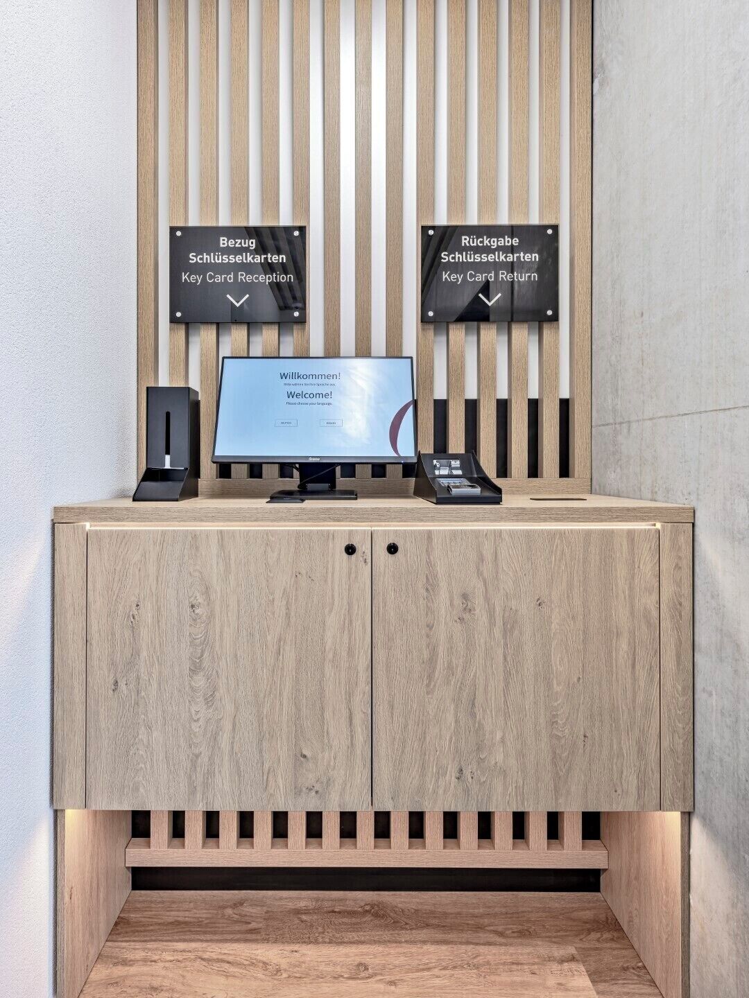 A reception desk with a computer monitor, a keyboard, and a remote control. There are signs above the desk indicating 'Key Card Reception' and 'Key Card Return'.