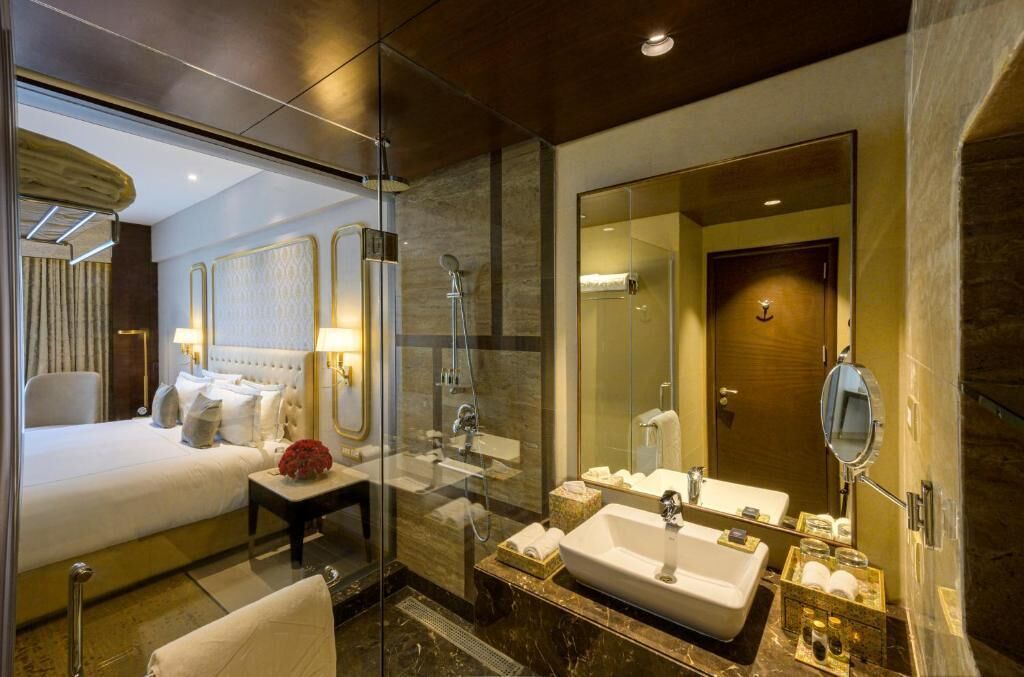 Une chambre d’hôtel moderne dotée d’une douche en verre, d’un grand lit, d’une coiffeuse avec un miroir et d’une salle de bain séparée.