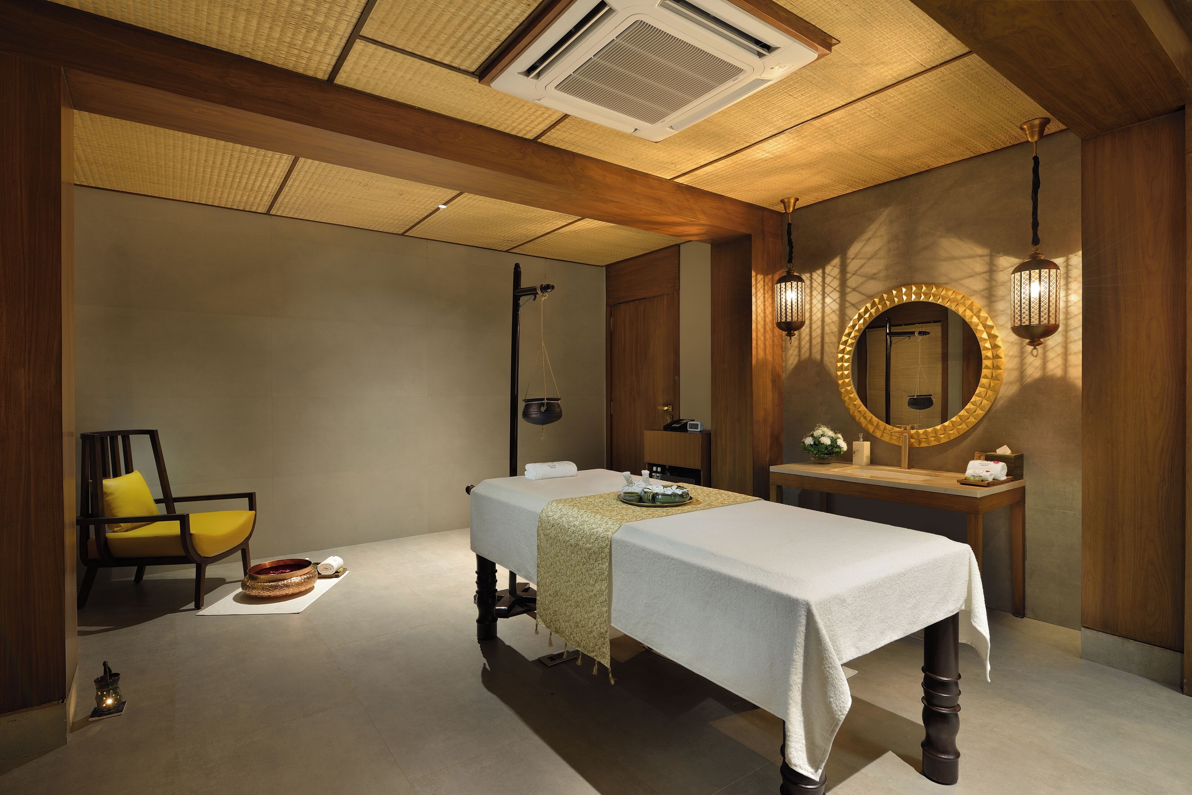 A spa room with a massage table, a wooden chair, a mirror, and a small table with a candle.