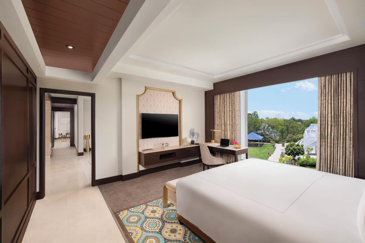 A hotel room with a large bed, a desk with a computer, a TV, and a view of the outdoors.