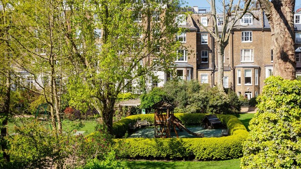 A well-maintained garden with a play area, neatly trimmed hedges, and a brick building in the background. - Light Show, by Veeve (London)