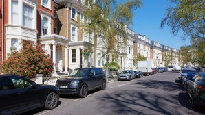 A row of terraced houses with parked cars on the street. - Light Show, by Veeve (London)