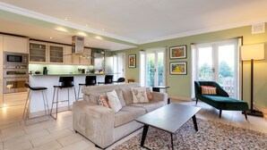 A modern kitchen with a dining area, a sofa, and a green chair. - Light Show, by Veeve (London)
