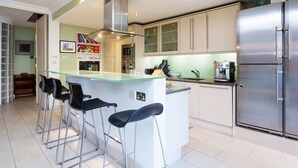 A modern kitchen with a central island, bar stools, stainless steel appliances, and light-colored cabinetry. - Light Show, by Veeve (London)