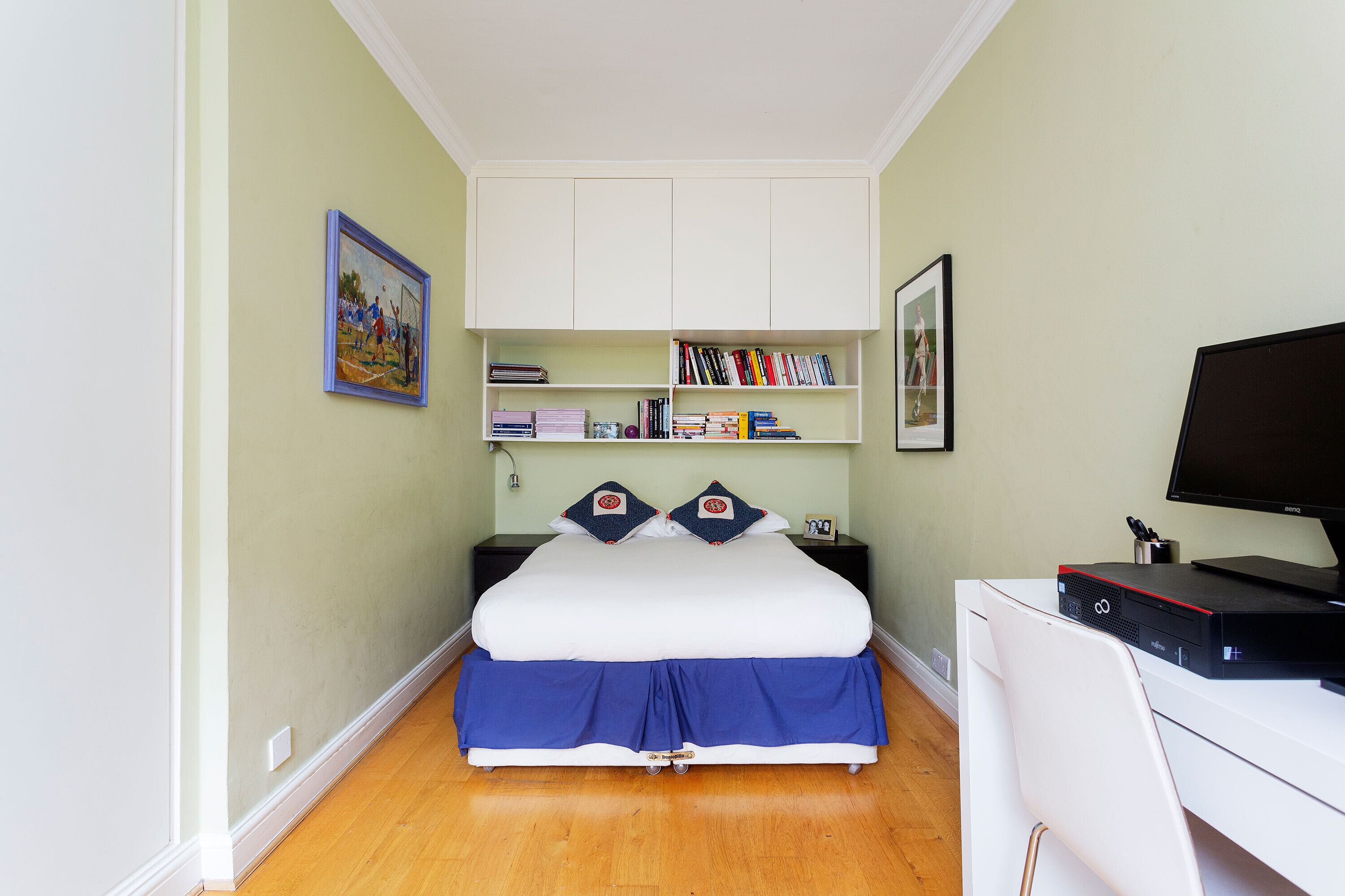 Una camera da letto con un letto, comodini, una scrivania con un computer e mensole con libri e oggetti decorativi.