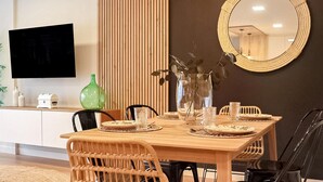 A dining area with a wooden table set for four, surrounded by wicker chairs. A large mirror hangs on the wall, and a flat-screen TV is mounted above the table. - Stunning apartment in Vimianzo with WiFi (Vimianzo)
