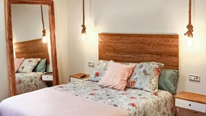 A bedroom with a wooden headboard, floral bedding, a large mirror, bedside tables, and wall-mounted lights. - Stunning apartment in Vimianzo with WiFi (Vimianzo)