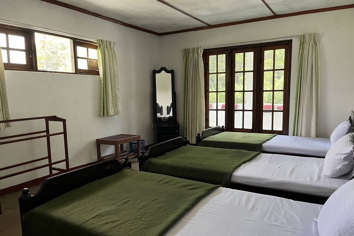 Una habitación con dos camas individuales, un banco de madera, un espejo y una ventana con cortinas.