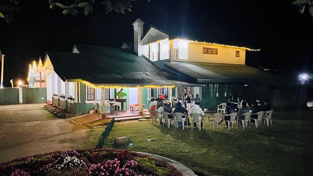 Un área de estar al aire libre con mesas y sillas, un escenario con un piano y un edificio de fachada amarilla.