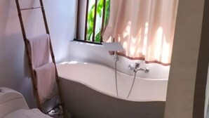 Un baño con bañera, una ventana con vistas a la vegetación y un perchero para toallas.