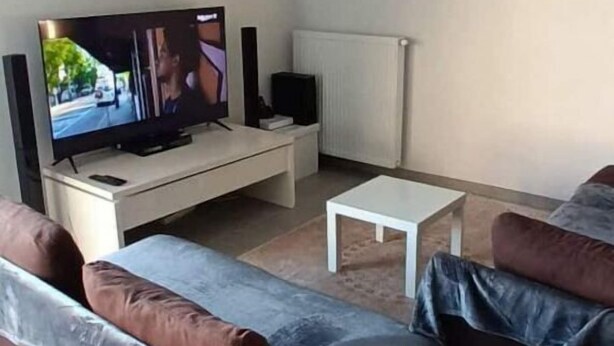Een moderne woonkamer met een flatscreen televisie, een witte salontafel en twee banken met kussens.