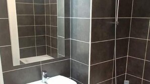 Een badkamer met donkere betegelde wanden, een witte wastafel, een spiegel en een bad.