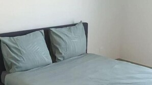 Een enkel bed met een grijze matras en bijpassende kussens, een donker hoofdbord en een betegelde vloer.
