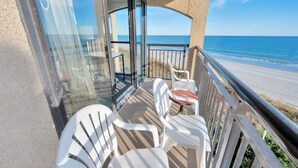 A balcony with white plastic chairs and a small table, overlooking a beach and the ocean. - New Corner Direct Oceanfront View - 5th Floor - Pools (North Myrtle Beach)