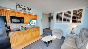 A compact living space with a kitchenette, a sofa, a small table, and a window with blinds. - New Corner Direct Oceanfront View - 5th Floor - Pools (North Myrtle Beach)