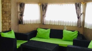 Ein Wohnzimmer mit einer Sofagarnitur und einem Couchtisch, einer Steinwand und Fenstern mit Vorhängen.