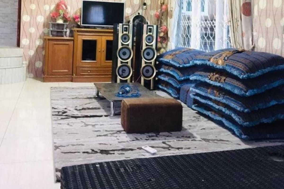 Een woonkamer met een televisie, speakers, een bank en een behang met patroon.