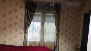 Ein Schlafzimmer mit Bett, Vorhängen, einer Pendelleuchte und blumigem Wandpapier.
