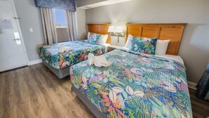 Une chambre d’hôtel avec deux lits, chacun agrémenté d’une literie à motifs floraux, d’une tête de lit en bois et d’une fenêtre avec des rideaux.