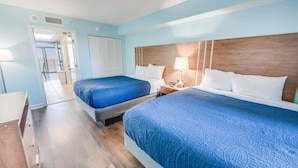 Habitación de hotel con dos camas, cabecero de madera y vista al balcón.