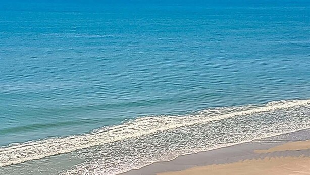 Een strand met helderblauw water en een zandstrand.
