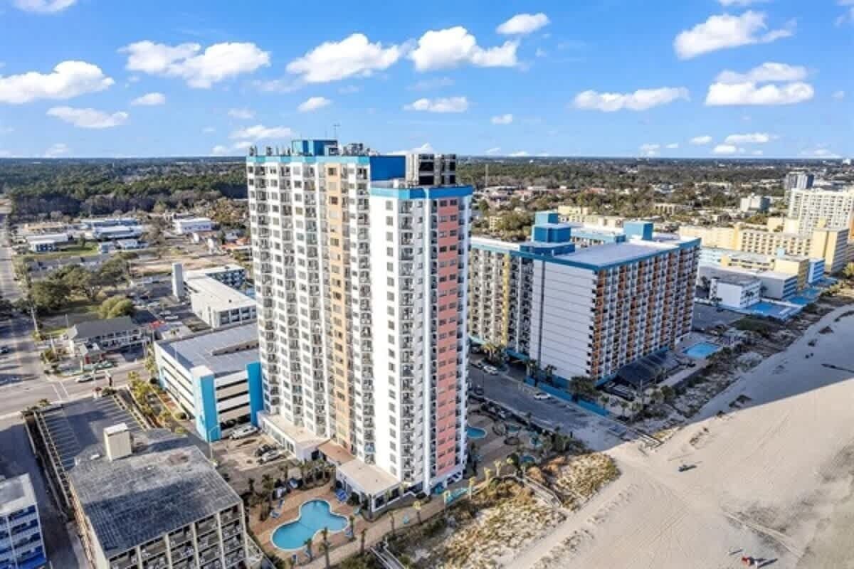 Un hotel de altura con varias plantas, una zona de piscina y vistas a la playa.