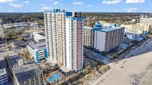 Een hoog hotel met meerdere verdiepingen, een zwembad en uitzicht op het strand.